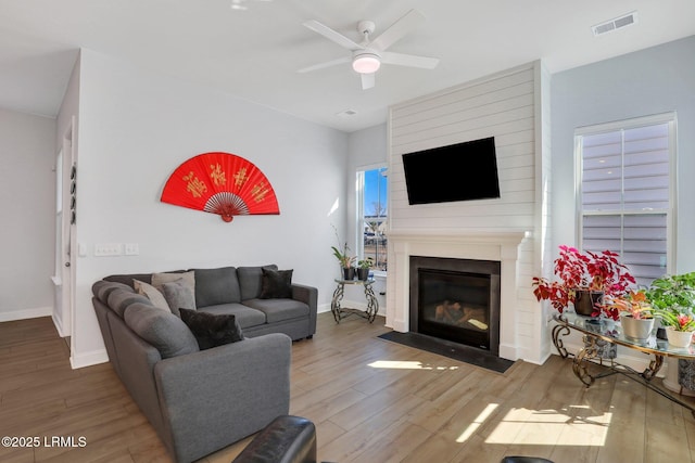 living area with a large fireplace, baseboards, visible vents, and wood finished floors