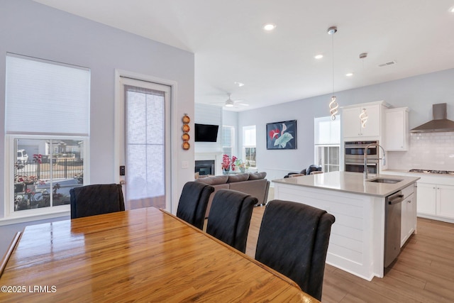 dining room featuring light wood-style floors, a glass covered fireplace, recessed lighting, and a ceiling fan