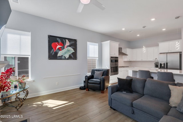 living area with a ceiling fan, recessed lighting, baseboards, and light wood finished floors