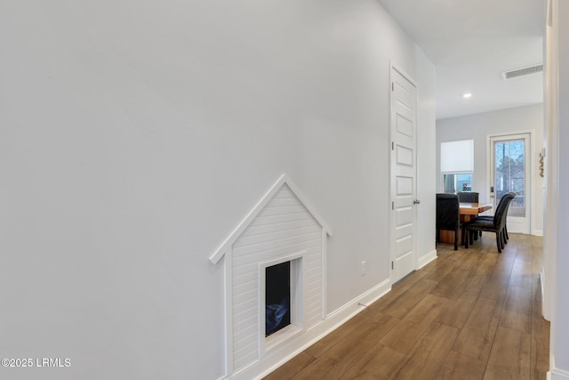 hallway with wood finished floors, visible vents, and baseboards