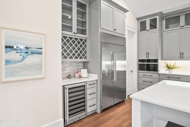 kitchen with gray cabinets, backsplash, wine cooler, light stone counters, and stainless steel built in fridge