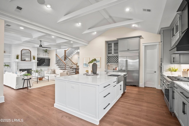 kitchen featuring sink, high quality appliances, an island with sink, hardwood / wood-style flooring, and wall chimney range hood