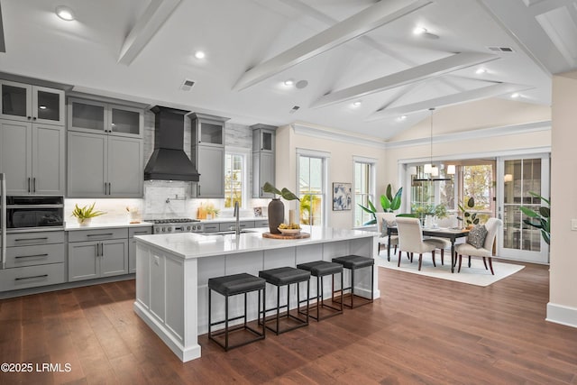 kitchen with sink, gray cabinets, a center island with sink, a kitchen bar, and custom exhaust hood