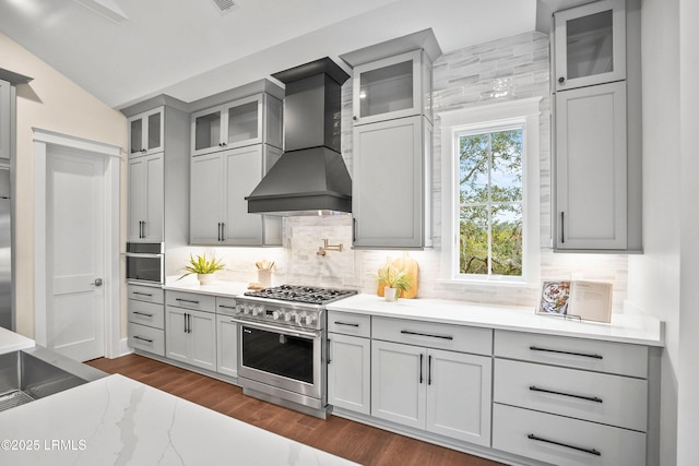 kitchen with tasteful backsplash, high end stainless steel range, vaulted ceiling, and custom exhaust hood