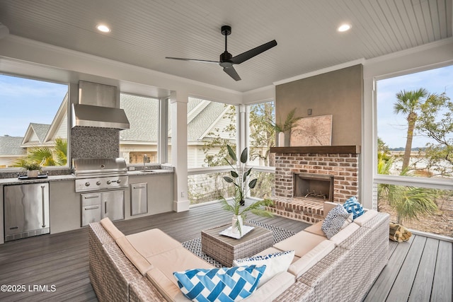 wooden deck with sink, ceiling fan, a grill, an outdoor living space with a fireplace, and exterior kitchen