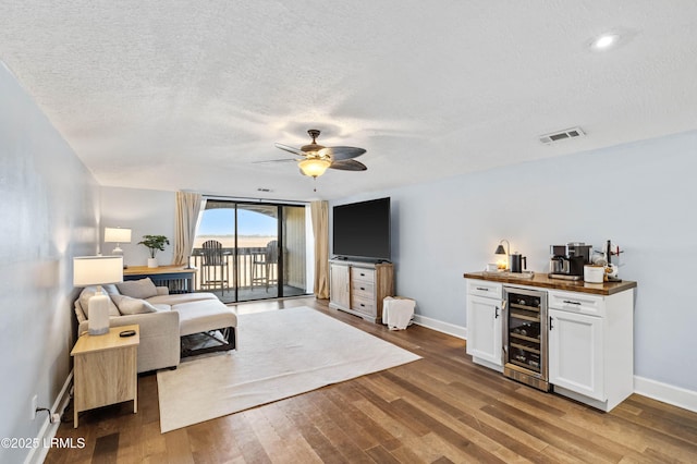 living room with hardwood / wood-style flooring, beverage cooler, a textured ceiling, and bar area