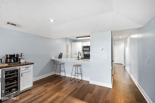 kitchen featuring a kitchen bar, sink, white cabinetry, dark hardwood / wood-style flooring, and beverage cooler