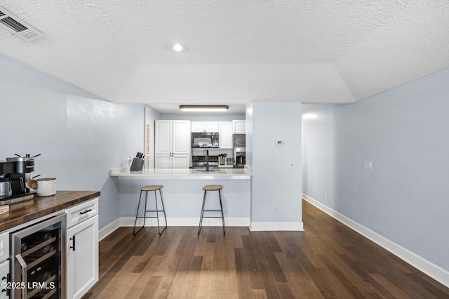 kitchen featuring wine cooler, stainless steel fridge with ice dispenser, a textured ceiling, a kitchen breakfast bar, and white cabinets