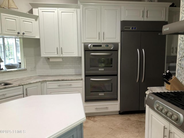 kitchen with gas cooktop, built in fridge, dobule oven black, white cabinets, and ventilation hood