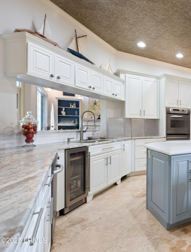 kitchen featuring beverage cooler, white cabinets, a sink, and oven