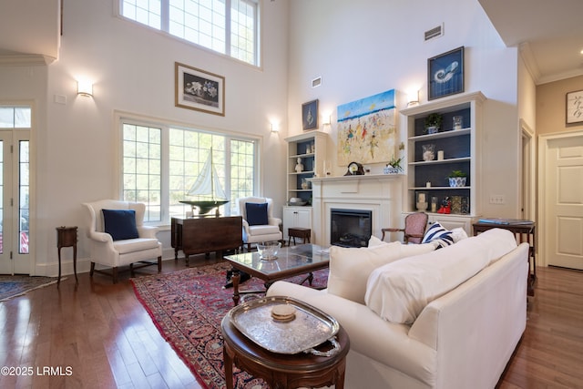 living area featuring crown molding, visible vents, a high ceiling, a glass covered fireplace, and wood finished floors