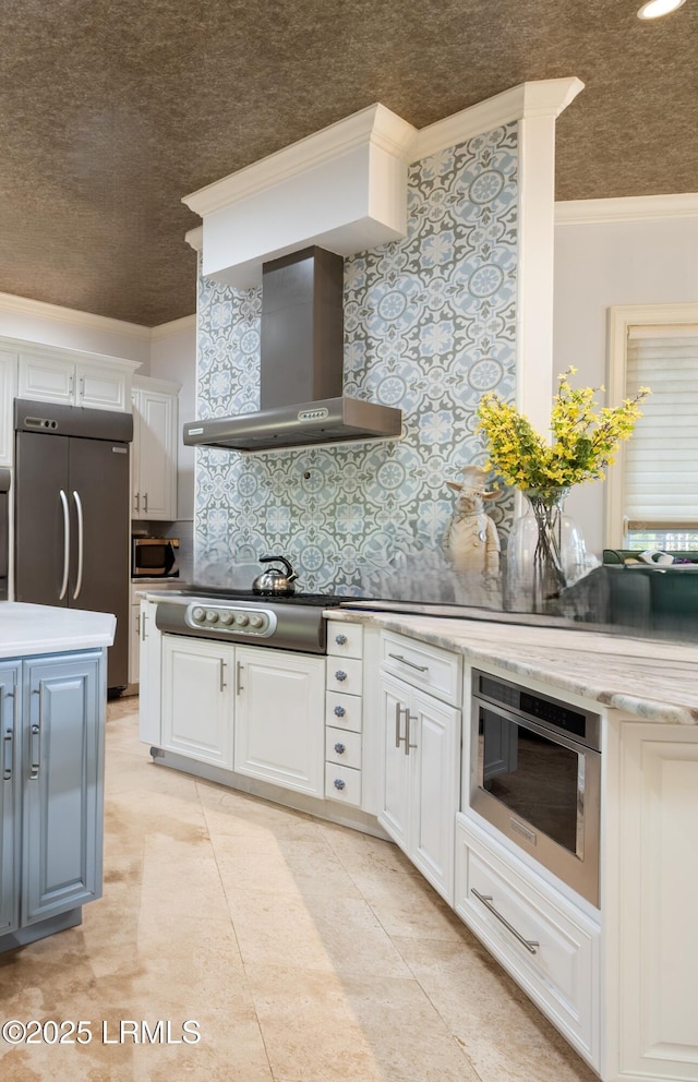 kitchen featuring wall chimney range hood, appliances with stainless steel finishes, white cabinets, and ornamental molding