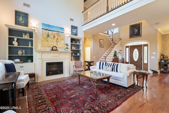 living area featuring built in features, a fireplace, visible vents, wood finished floors, and stairs