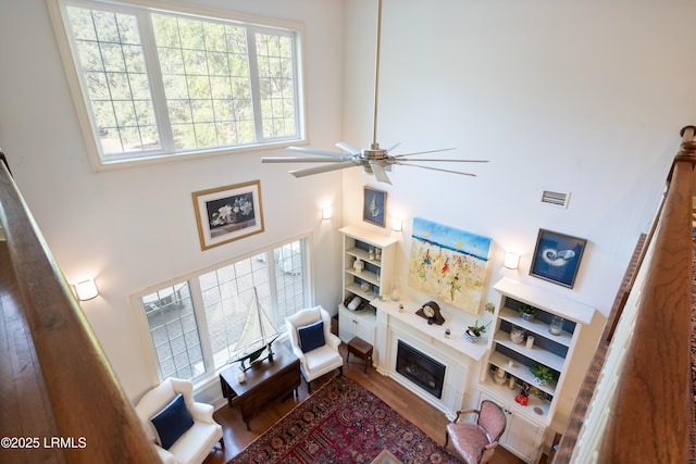 living area featuring visible vents, a ceiling fan, a towering ceiling, wood finished floors, and a fireplace