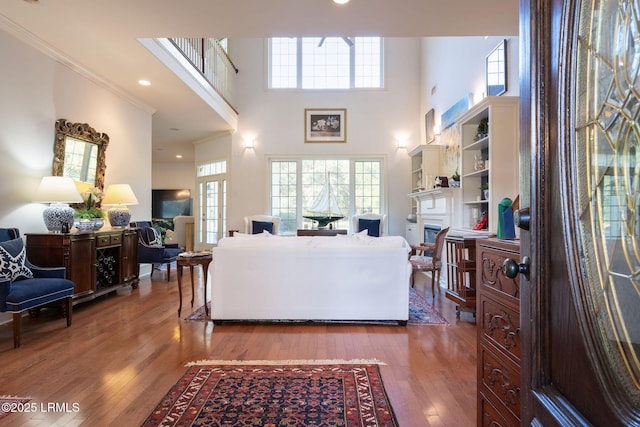 living area with a fireplace, wood-type flooring, a towering ceiling, and crown molding