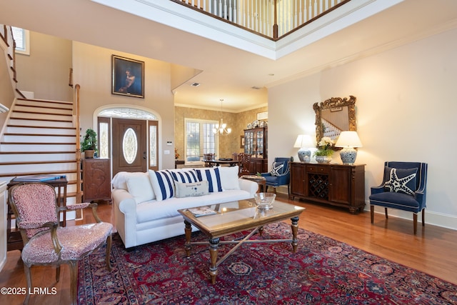 living room featuring a towering ceiling, wood finished floors, stairs, crown molding, and a notable chandelier