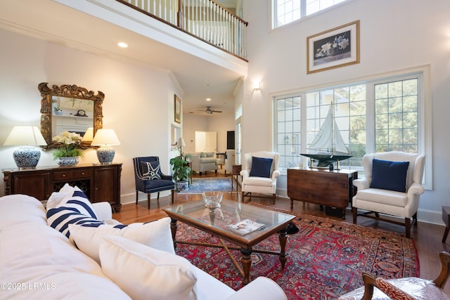 living room with a towering ceiling, crown molding, baseboards, and wood finished floors