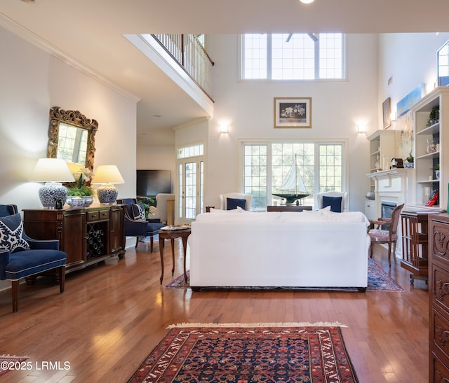 living area featuring wood-type flooring, a glass covered fireplace, a towering ceiling, and crown molding