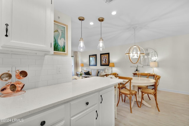 kitchen featuring tasteful backsplash, light stone counters, decorative light fixtures, light hardwood / wood-style flooring, and white cabinets