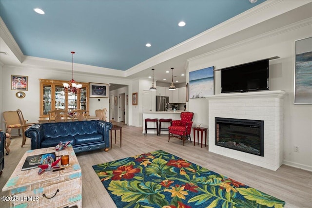 living room featuring crown molding, a brick fireplace, light hardwood / wood-style flooring, and a tray ceiling