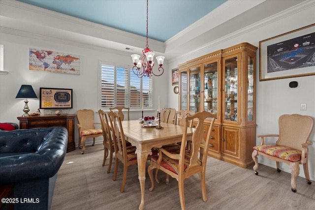 dining area featuring a raised ceiling, ornamental molding, a chandelier, and light hardwood / wood-style flooring