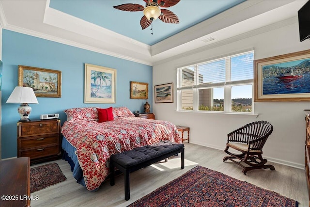 bedroom with crown molding, a raised ceiling, ceiling fan, and light wood-type flooring