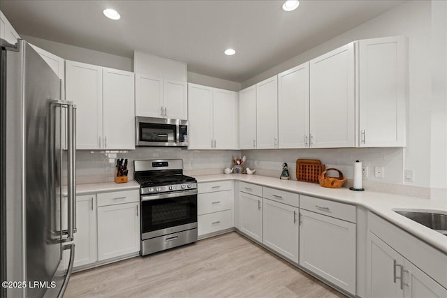 kitchen with stainless steel appliances, white cabinetry, tasteful backsplash, and light hardwood / wood-style floors