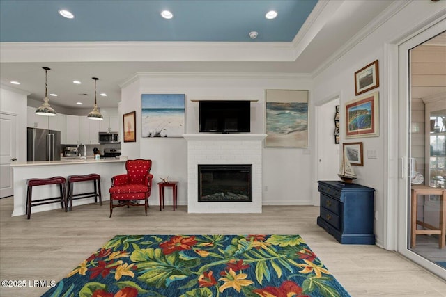 living room with a brick fireplace, crown molding, light hardwood / wood-style floors, and sink