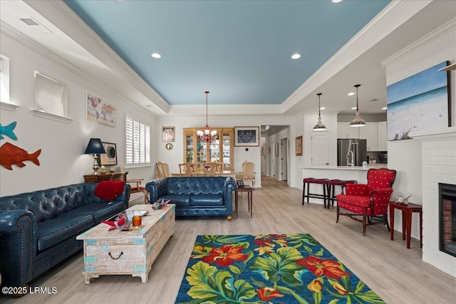 living room featuring an inviting chandelier, ornamental molding, a brick fireplace, and light wood-type flooring