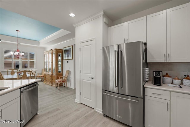 kitchen featuring white cabinetry, an inviting chandelier, hanging light fixtures, a tray ceiling, and stainless steel appliances