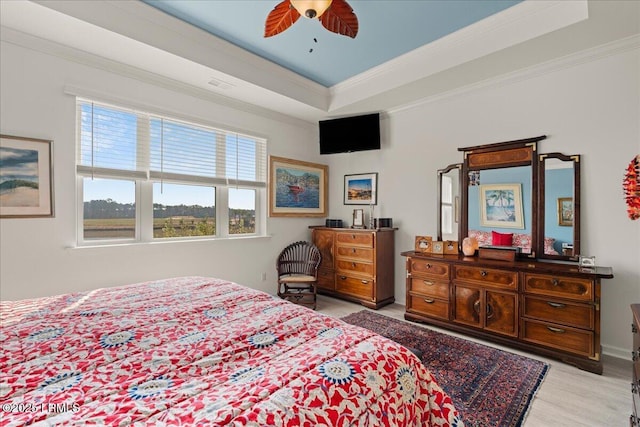 bedroom with ornamental molding, ceiling fan, light hardwood / wood-style floors, and a tray ceiling