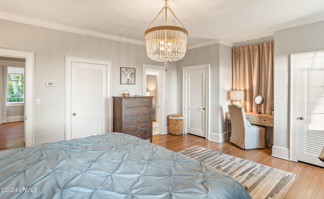 bedroom featuring crown molding, a notable chandelier, two closets, and light hardwood / wood-style floors