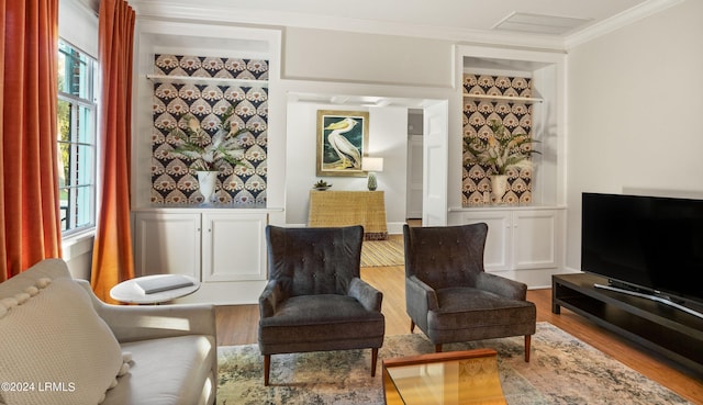 sitting room with built in shelves, light hardwood / wood-style flooring, and ornamental molding