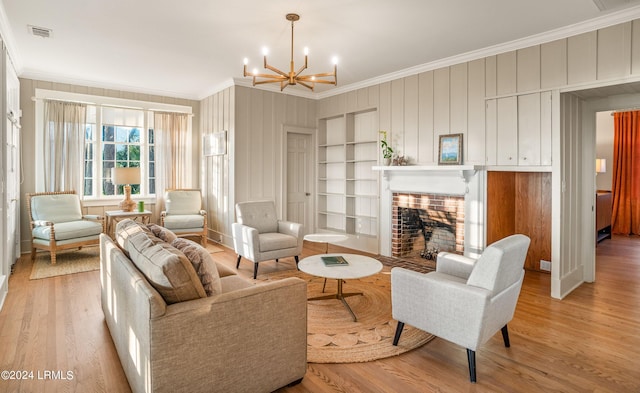 living room featuring a notable chandelier, ornamental molding, a brick fireplace, built in shelves, and light wood-type flooring