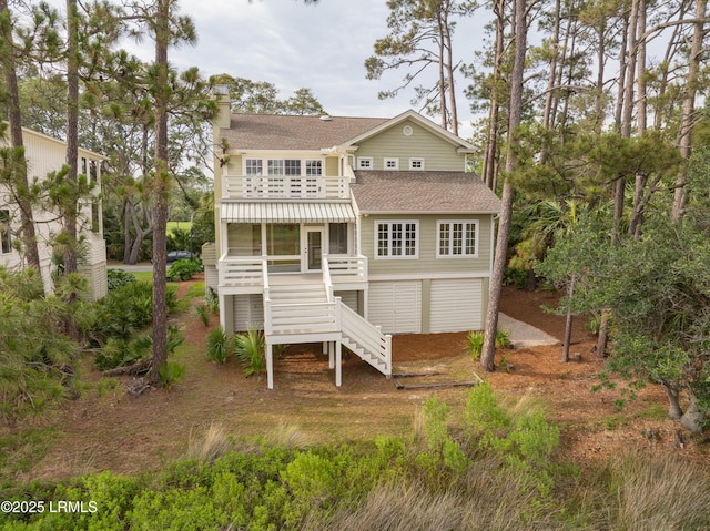 rear view of house featuring stairs, roof with shingles, a chimney, and a sunroom
