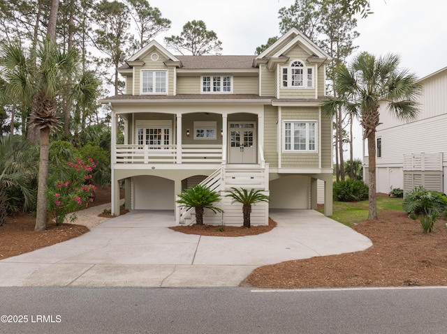 coastal inspired home featuring concrete driveway, a carport, an attached garage, a porch, and stairs