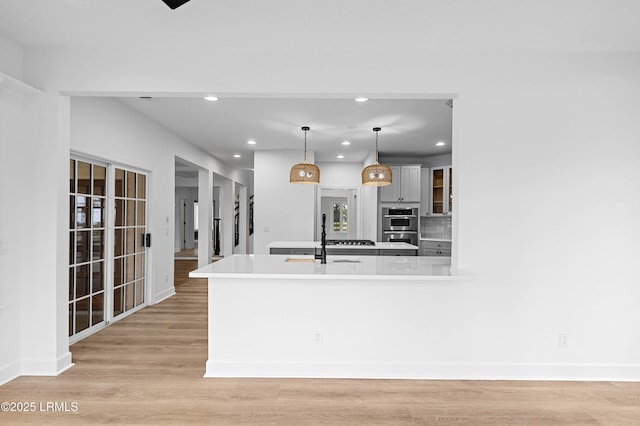 kitchen with a sink, double oven, recessed lighting, baseboards, and light wood-style flooring