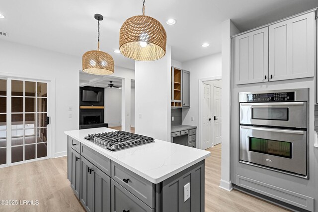 kitchen featuring appliances with stainless steel finishes, gray cabinetry, a ceiling fan, light wood-style flooring, and light stone countertops