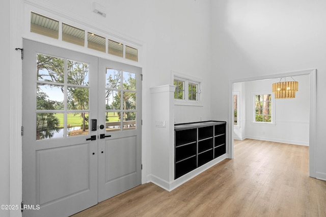 entryway with a towering ceiling, plenty of natural light, a chandelier, light wood-style flooring, and baseboards