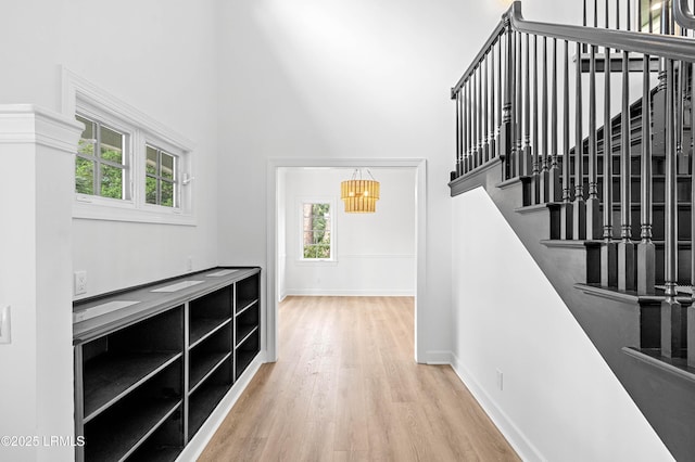 hall with a high ceiling, wood finished floors, healthy amount of natural light, a chandelier, and stairway