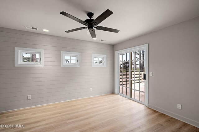 unfurnished room featuring wood finished floors, healthy amount of natural light, a ceiling fan, baseboards, and wood walls