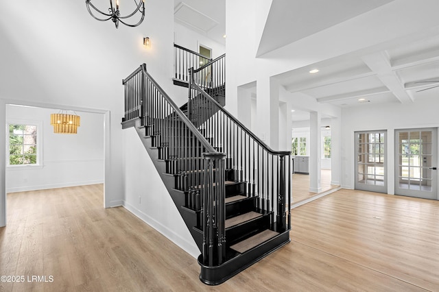 stairs featuring a chandelier, wood finished floors, baseboards, beamed ceiling, and a high ceiling