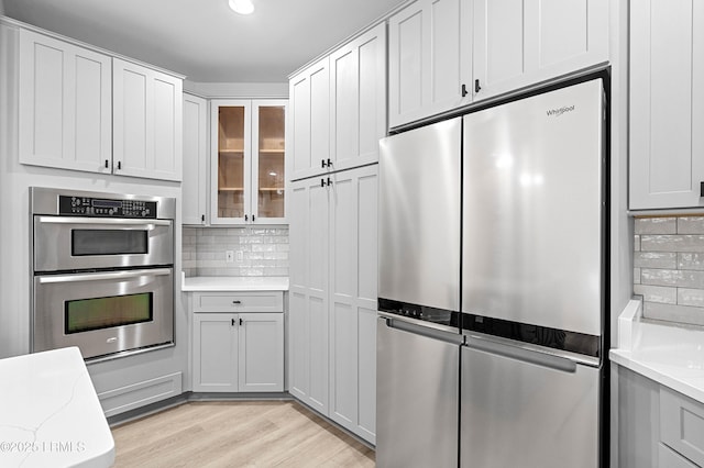kitchen featuring stainless steel appliances, tasteful backsplash, glass insert cabinets, and light wood-style floors