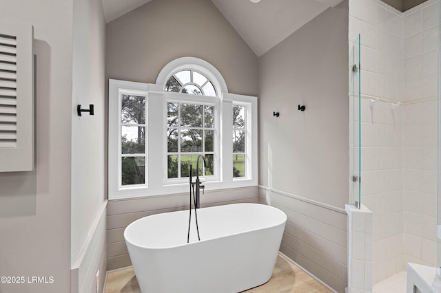 bathroom with a freestanding tub, a walk in shower, wainscoting, and lofted ceiling