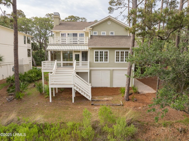rear view of property with stairway, roof with shingles, a chimney, a deck, and a sunroom