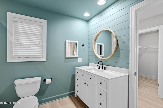 bathroom featuring wood finished floors, toilet, baseboards, vanity, and recessed lighting