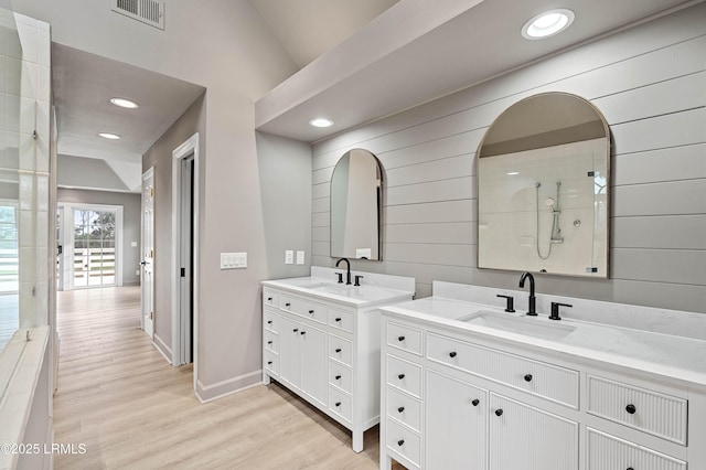 bathroom featuring wooden walls, wood finished floors, baseboards, two vanities, and recessed lighting