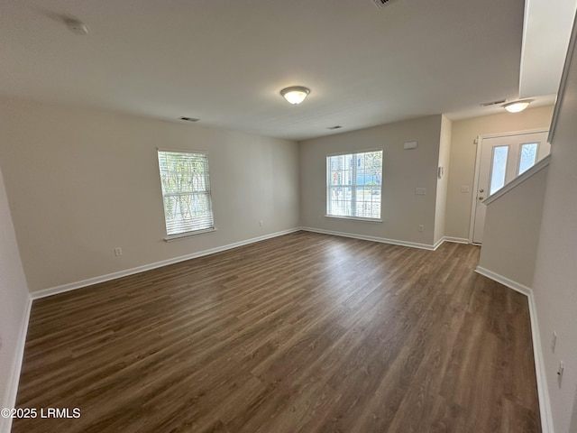 empty room featuring baseboards, dark wood-type flooring, visible vents, and a healthy amount of sunlight