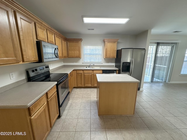 kitchen with appliances with stainless steel finishes, a kitchen island, a sink, and light tile patterned floors