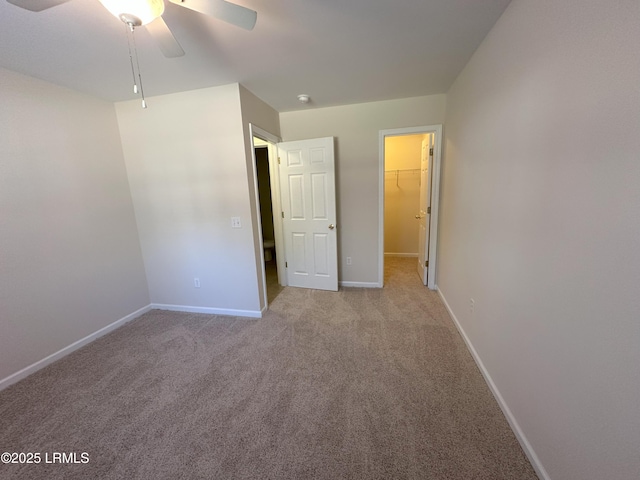 unfurnished bedroom with carpet floors, a walk in closet, a closet, a ceiling fan, and baseboards